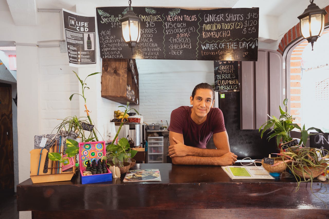Cozy cafe scene featuring a friendly barista behind the counter with a menu board and potted plants.